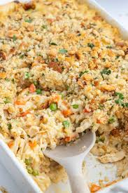 Baked casserole with a golden breadcrumb topping and visible peas and carrots, being scooped with a white spoon.
