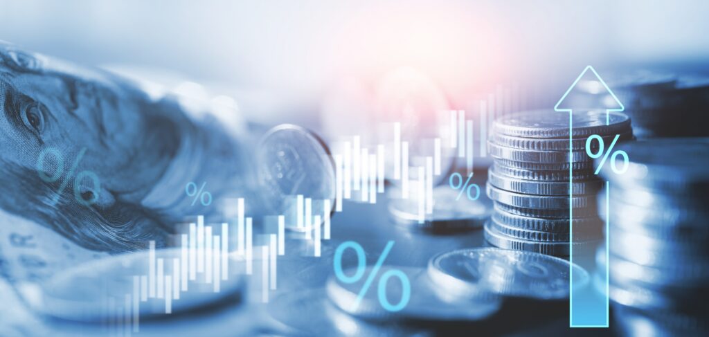 Stacked coins and U.S. currency overlaid with digital graphics showing an upward arrow, percentage symbols, and a rising candlestick chart, symbolizing increasing interest rates or inflation.